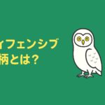 ディフェンシブ銘柄をテーマにした緑と黄色のアイキャッチ画像。中央に「ディフェンシブ銘柄とは？」という黄色の日本語テキストと、右側にやさしい表情のフクロウのイラストが配置されている。初心者向けの安心感を表現したデザイン。